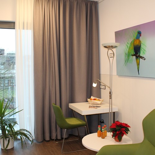 Blick in ein freundliches Patientenzimmer mit Tisch, Stuhl, Beleuchtung und Gardine