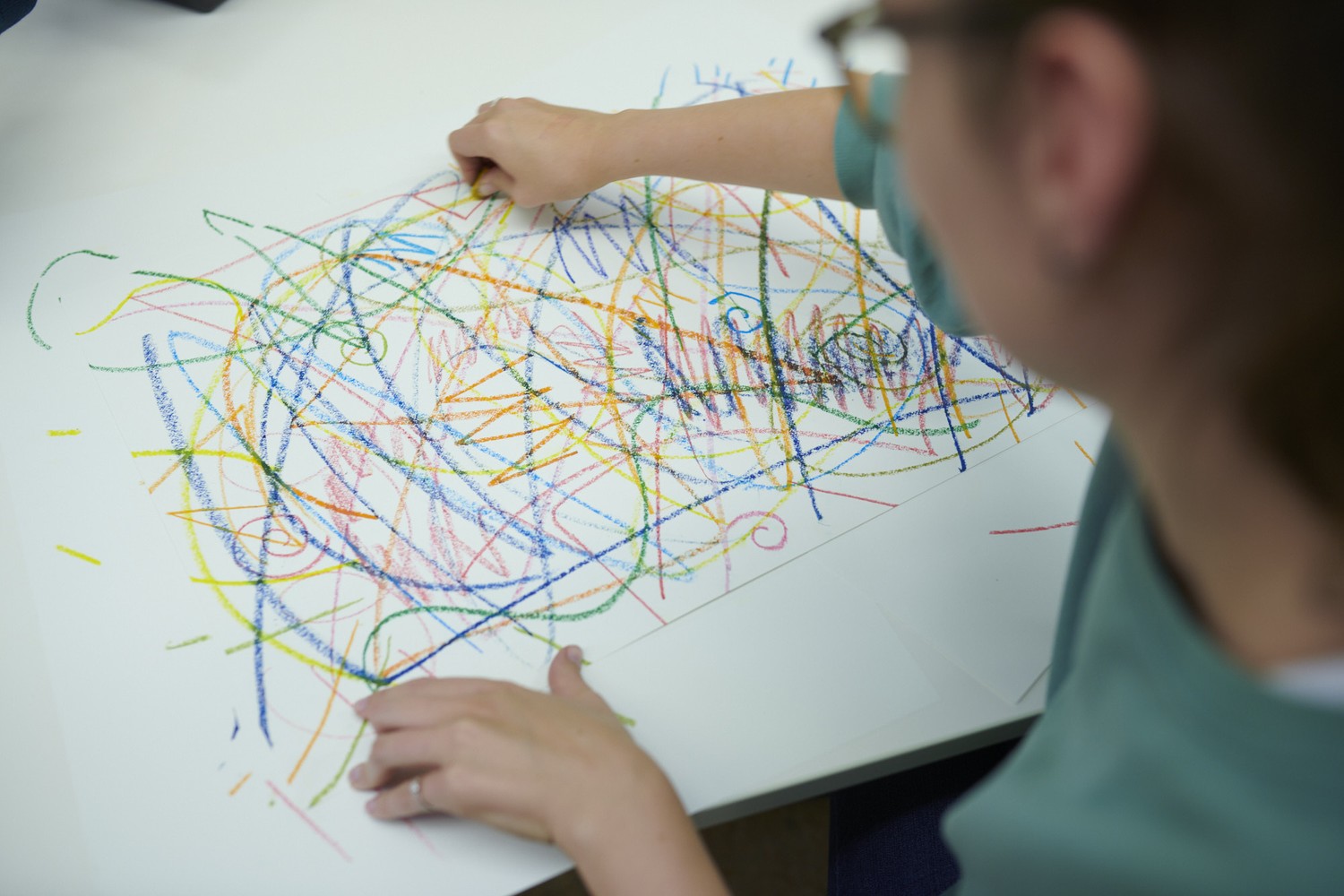 Patientin malt abstrakte Muster mit Wachskreide auf Papier.
