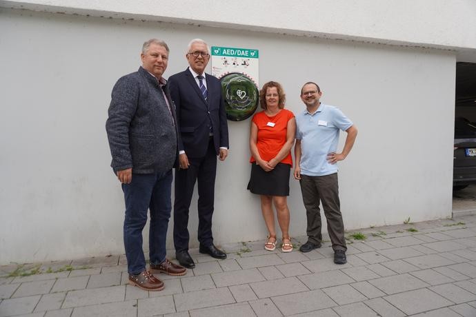 Stehen neben dem öffentlich zugänglichen Defibrillator (AED), der an Wand der LWL-Tagesklinik Plettenberg hängt.
