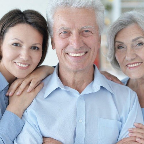 Zwei Frauen mittlere und fortgeschrittenen Alters umarmen lachend einen älteren Mann