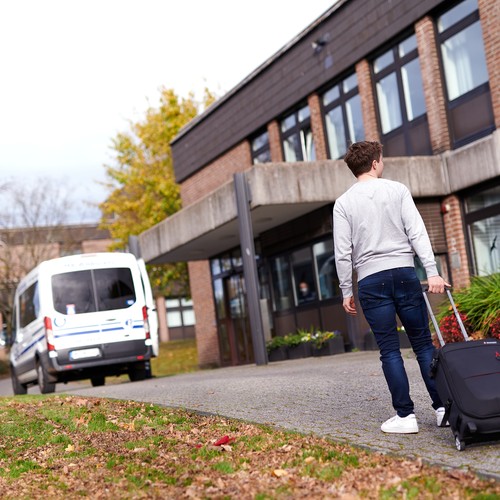 Ein junger Mann mit Koffer steht vor der zentralen Aufnahme der LWL-Klinik Hemer.