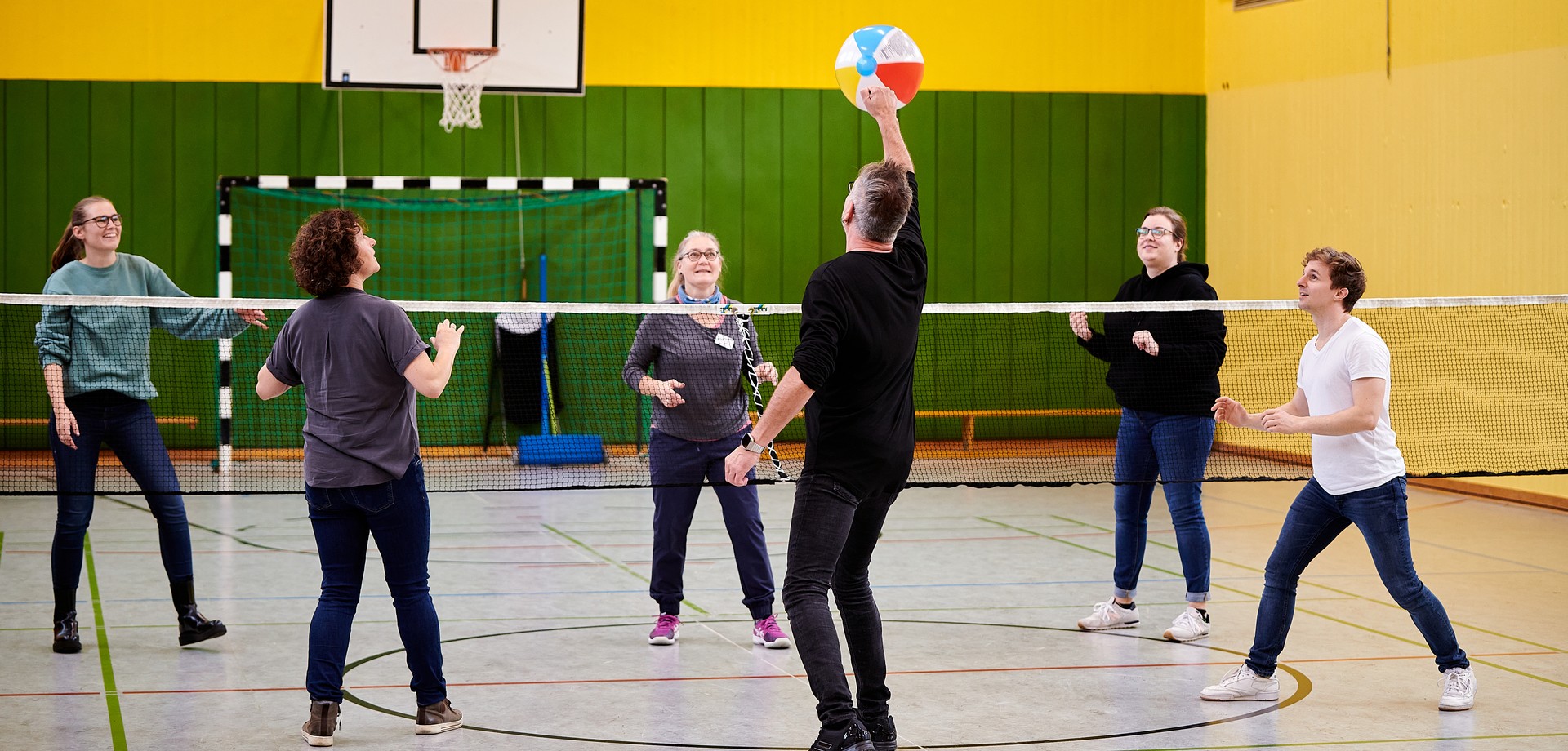 Sechs Personen spielen über ein Netz hinweg mit einem Ball