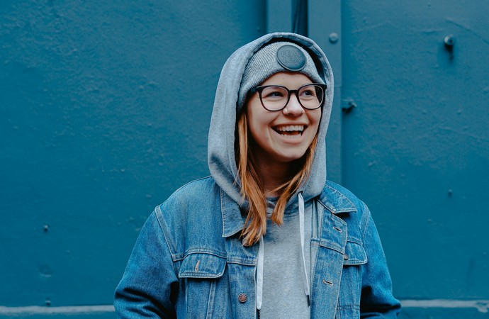 Junge Frau mit Jeansjacke und Mütze steht vor einer blauen Eisenwand
