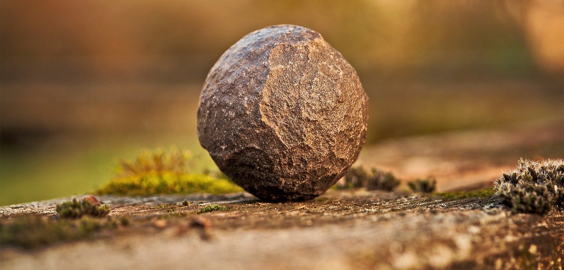 Ein großer, kugelrunder Stein mit einigen Macken liegt auf einer Steinplatte auf dem Boden