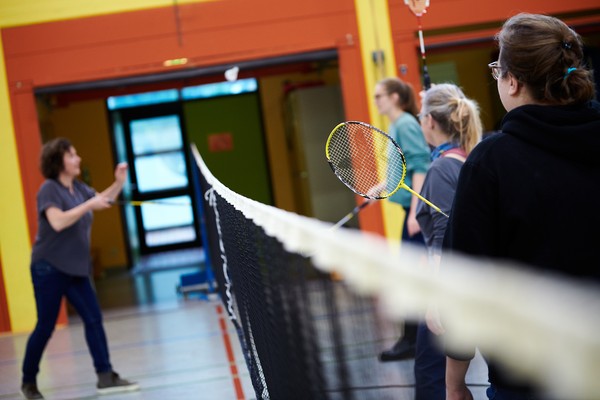 Personen stehen mit Federballschlägern um ein gespanntes Tennisnetz