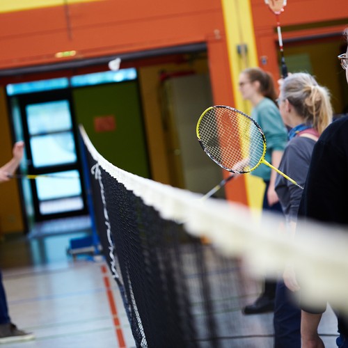 Mehrere Personen stehen mit Federballschlägern neben einem gespannten Tennisnetz
