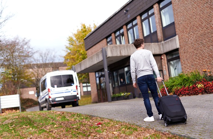 Junger Mann mit Koffer steht vor der Zentralen Anmeldung der LWL-Klinik Hemer.