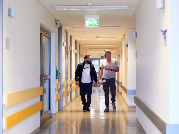 Zwei Mitarbeiter gehen über den Gang der Station C9. (vergrößerte Bildansicht wird geöffnet)