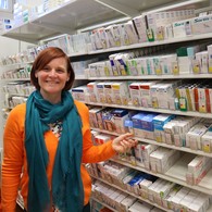 Eine Frau steht vor einem Medikamentenregal und lächelt freundlich in die Kamera