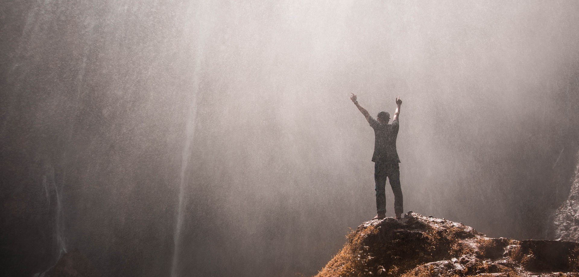 Mann vor Wasserfall, reißt die Hände hoch