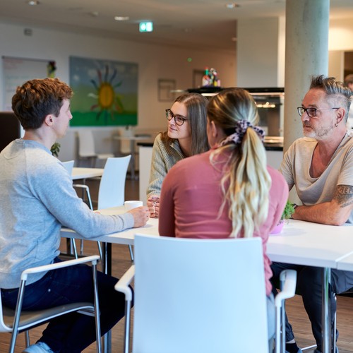 Personen sitzen an einem Tisch und unterhalten sich miteinander